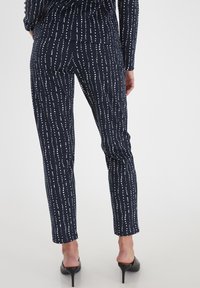 Pantalones marinos con rayas verticales blancas, de corte slim y textura suave, combinados con tacones altos negros.