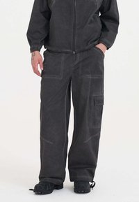 Pantaloni cargo realizzati in un tessuto textured color carbone, con numerose tasche, una vestibilità comoda e dettagli di cucitura ben evidenti.
