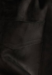 Primo piano di un tessuto scamosciato nero con una tasca posteriore visibile e dettagli di cucitura sottili. Texture liscia con una finitura opaca.