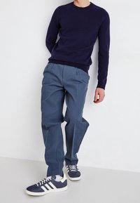 Marinblå stickad tröja, ljusblå smalnande byxor och marinblå sneakers med vita accenter. Avslappnad outfit med texturerad tyg och ledig passform.