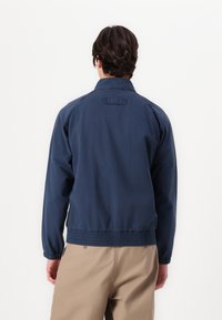 Τζάκετ σε ναυτικό μπλε χρώμα, ελαφρύ, με γιακά, ελαστικούς καρπούς και στρίφωμα, με ετικέτα στην πλάτη, φτιαγμένο από απαλό ύφασμα.