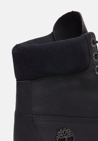 Must must, mille nahaga, voodri õmblused ja metallist logo aktsent. Disain sisaldab ümarat varba ja silmadega nööri.