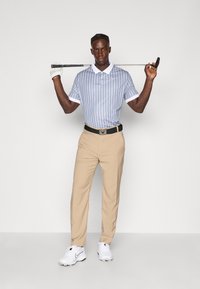 Conjunto de golfe com uma camisa polo listrada azul clara e colarinho branco, calças bege e sapatos de golfe brancos. Inclui um taco de golfe na mão.