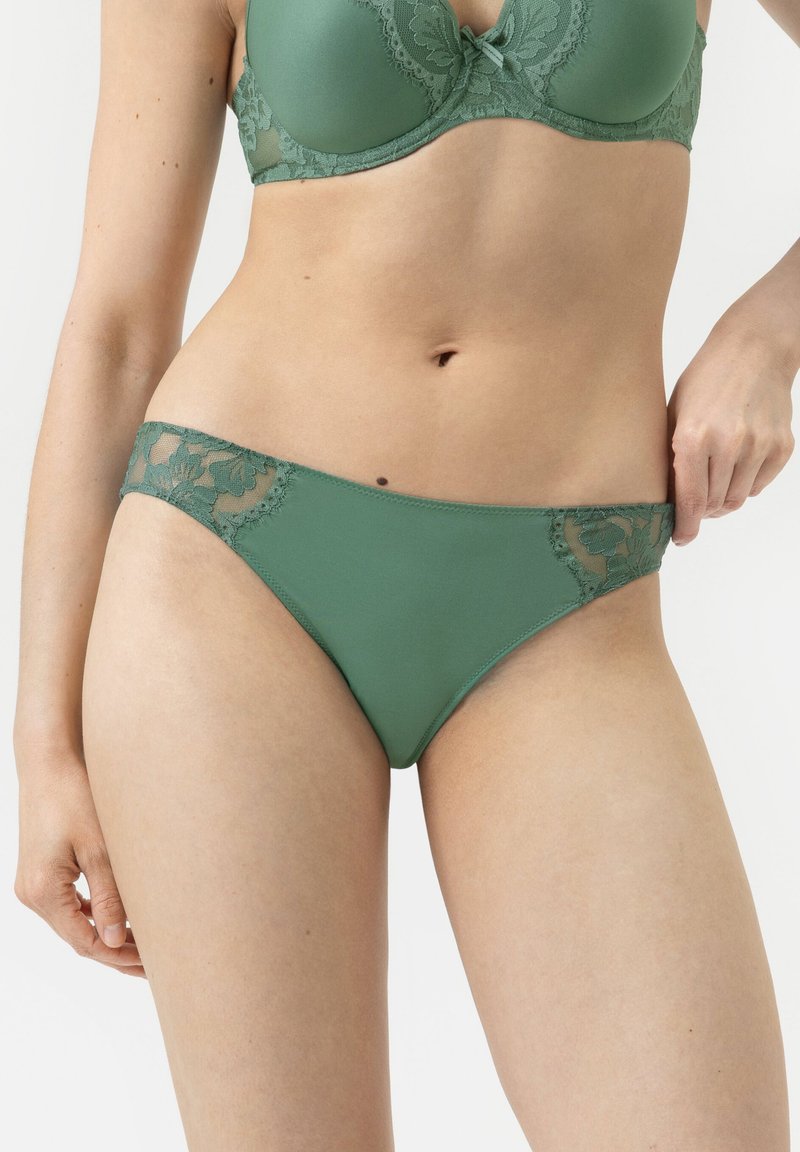 Grünes Lingerie-Set mit einem glatten, matten BH und passendem Bikinihöschen mit floralen Spitzeinsätzen an den Seiten.