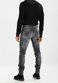 Šedé džíny z denimu s oprýskanými detaily a skvrnám od barvy na zadní straně. Slim fit design se standartními kapsami. Vhodné s černou obuví.