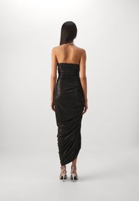Černé šaty bez ramínek s přiléhavým, řaseným designem. Měkká, lesklá látka s dlouhým siluetou. Pár stříbrně zdobených vysokých podpatků.