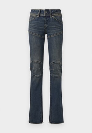 Sötétkék farmernadrág, amely szélesített fazonú, térdpárnákkal, fehér varrással és ezüst kiegészítőkkel rendelkezik. Cipzárral záródik a bokánál.