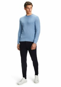 Pull en tricot bleu clair à manches longues avec un col rond, associé à un pantalon droit bleu marine et des baskets blanches. Texture douce sur l'ensemble.