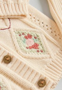 Strikket cremet cardigan med blomsterbroderi i pink og grøn, med teksturerede detaljer og træknapper.