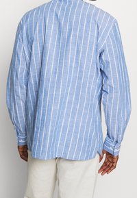 Camicia a maniche lunghe a righe blu chiaro in tessuto di lino, con strisce verticali bianche, polsini con bottoni e orlo arrotondato.