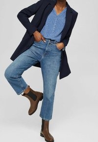 Blazer blu navy, blouse a pois blu, jeans chiari risvoltati e stivali alla caviglia marroni con lati elastici. Outfit semplice e moderno.