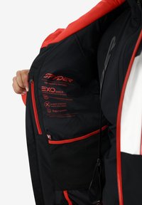 Giacca nera con dettagli rossi, dotata di etichette Exo Shield e Exo Thermo. Tasca interna in rete e coulisse regolabile per una vestibilità ottimale.