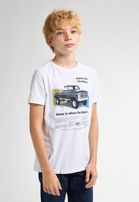 Hvid bomulds t-shirt med grafik af en sort vintage lastbil, tekst om Daytona 500 og en gul accent baggrund. Korte ærmer, rund hals.