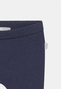 Navig blå ribbade leggings med en mjuk textur; de har en bred midja och en liten, grå logotagg på sidan för varumärkesidentifiering.