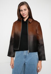 Braune und schwarze Gradient-Lederjacke mit einem Kragen, Reißverschluss vorne und cropped Ärmeln, kombiniert mit hellblauen Denim-Jeans.
