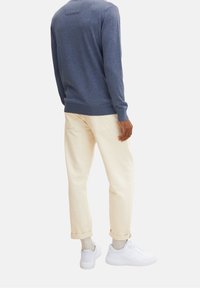 Mörkblå tröja med långa ärmar och ribbad nederkant, ihopparad med ljusbeiga byxor med uppvikta benslut och vita sneakers. Enkel, avslappnad design.