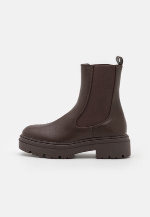 Bottine en cuir marron avec panneaux latéraux élastiques, surface texturée, et une semelle en caoutchouc dotée d'une semelle à crampons épaisse pour une meilleure adhérence.