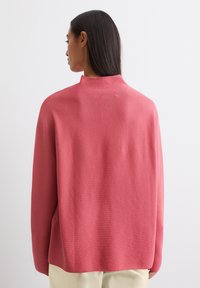 Roze gebreide trui met hoge kraag, relaxed fit en geribbeld patroon. Gladde afwerking, lange mouwen en licht gebogen zoom.