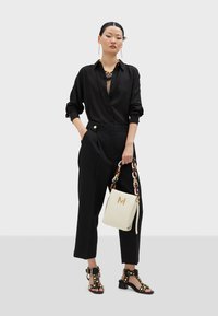 Black button-up shirt with subtle texture, high-waisted black trousers, strappy black sandals with studs, and a white handbag with a gold "M."