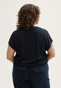 Top azul marino de manga corta con un patrón texturizado, combinado con pantalones de rayas y un corte relajado, visto desde atrás.