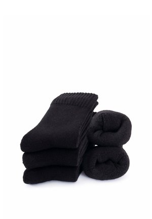 Drei gefaltete schwarze Socken, die neben zwei schwarzen Socken, die zu zylindrischen Formen gerollt sind, auf einem weißen Hintergrund gestapelt sind.