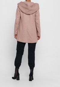 Pink hooded coat with a straight cut, long sleeves, and textured fabric. Paired with black cargo pants and heeled ankle boots.