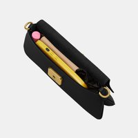 Μαύρη ορθογώνια τσάντα με χρυσά μεταλλικά στοιχεία που περιέχει ένα κίτρινο τηλέφωνο, μπεζ πορτοφόλι, ροζ λιπ μπαλμ και ένα μαύρο υφασμάτινο αντικείμενο μέσα.