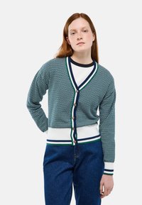 Cardigan tricoté en bleu marine et blanc avec un motif géométrique, encolure en V, fermeture boutonnée, et poignets et ourlet côtelés rayés contrastants.