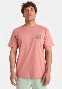 Roze katoenen T-shirt met een ronde hals en korte mouwen. Voorzien van een kleine, veelkleurige afbeelding op de linkerborst. Gladde textuur.