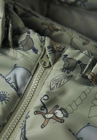Manteau rembourré en tissu vert clair avec des motifs animaliers et naturels. Comprend une fermeture éclair YKK et des accents cousus ; texture lisse et douce.