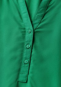 Camisa verde de botones con una textura de satén suave, cinco botones a juego y un diseño clásico de cuello en V con costuras en el cuello.