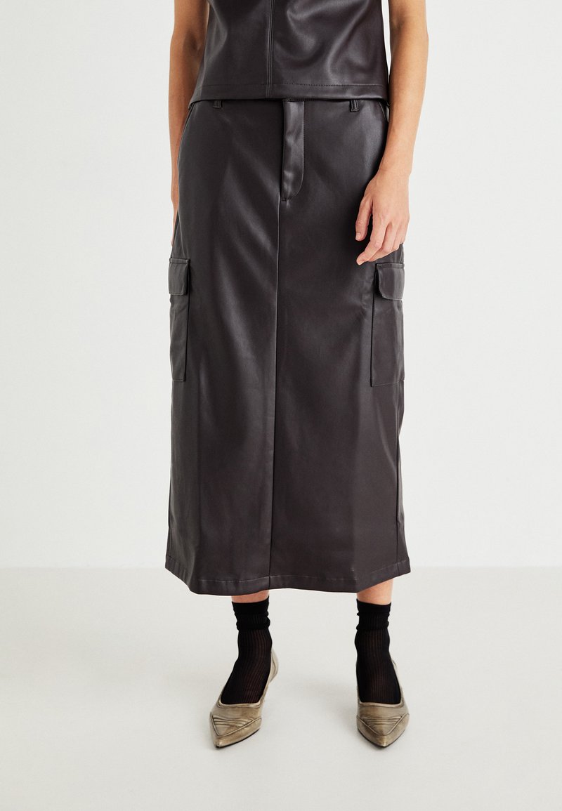 Svart skinn midi-skjørt med rett snitt og sidelommer, paret med beige spisse sko og svarte ankelstrømper.