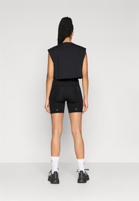 Crni skraćeni top bez rukava s šavovima na ramenima, uparen s crnim uskim kratkim hlačama s bočnim džepovima i malim bijelim detaljima.