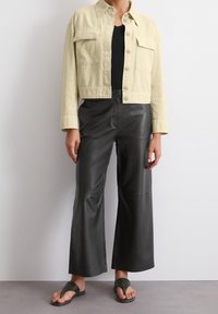 Light beige cropped jacket with two chest pockets, paired with black wide-leg leather pants. Flat sandals complete the outfit.