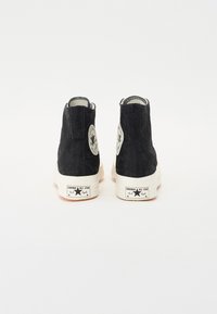 Zapatillas altas negras con textura de cordones, suelas de goma blanca y un parche con logo circular que presenta una estrella en el costado.
