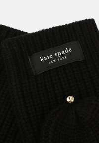 Svart stickad tyg med ribbat mönster, med en svart etikett som läser "kate spade NEW YORK" och en gyllene dekorativ knapp.