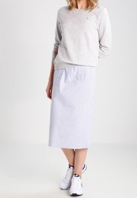 Sudadera gris, falda midi de rayas blancas y azules, zapatillas blancas. La falda tiene un bolsillo trasero y un diseño de corte recto.