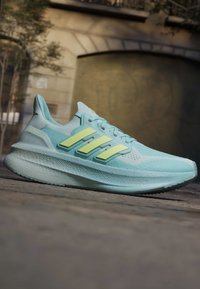 Hele sinine Adidas Ultraboost jooksujalanõu kollaste triipudega, mis puhkab väljas kivist sillutisel.