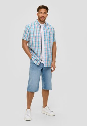 Korte mouwen geruite shirt in blauw, roze en groen; gecombineerd met lichtblauwe denim shorts; vergezeld door witte sneakers.