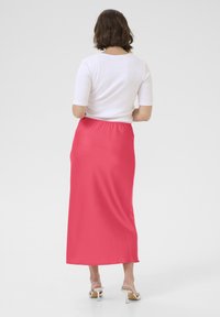 Falda maxi rosa hecha de un tejido suave con una cintura elástica, combinada con una blusa blanca ajustada. Diseño simple, sin patrones o detalles visibles.