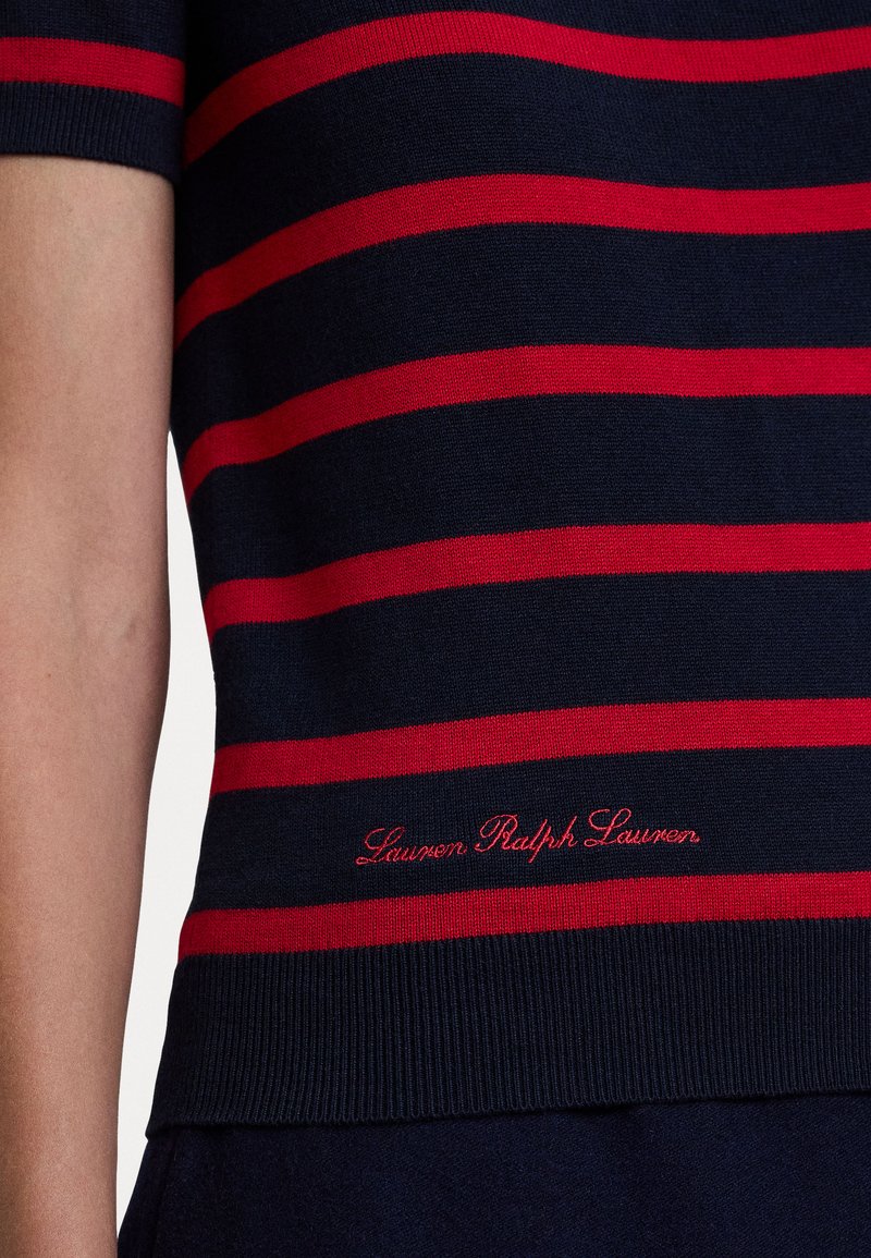 Top in maglina blu navy con righe orizzontali rosse. Presenta maniche corte e logo ricamato "Lauren Ralph Lauren" sull'orlo.