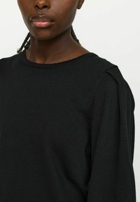Maglione nero a maglia con scollo rotondo, tessuto testurizzato e dettagli sottili sulle spalle. Inquadratura ravvicinata della parte superiore del torso.