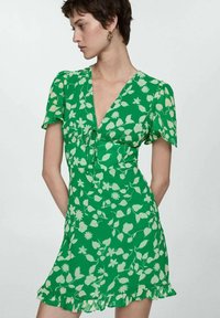 Rochie florală verde cu mâneci scurte și voluminoase, având detaliu cu funda la gât și marginile ondulate. Fabricată dintr-un material ușor și fluid.