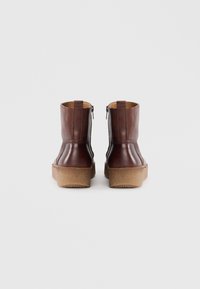 Botas de cuero marrón hasta el tobillo con acabado texturizado, que presentan una puntera redondeada, cierre de cremallera y una suela de plataforma gruesa y de color claro.