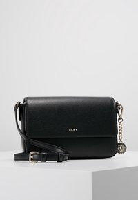 Black leather crossbody bag with textured finish, gold hardware, adjustable strap, and a decorative DKNY charm attached.