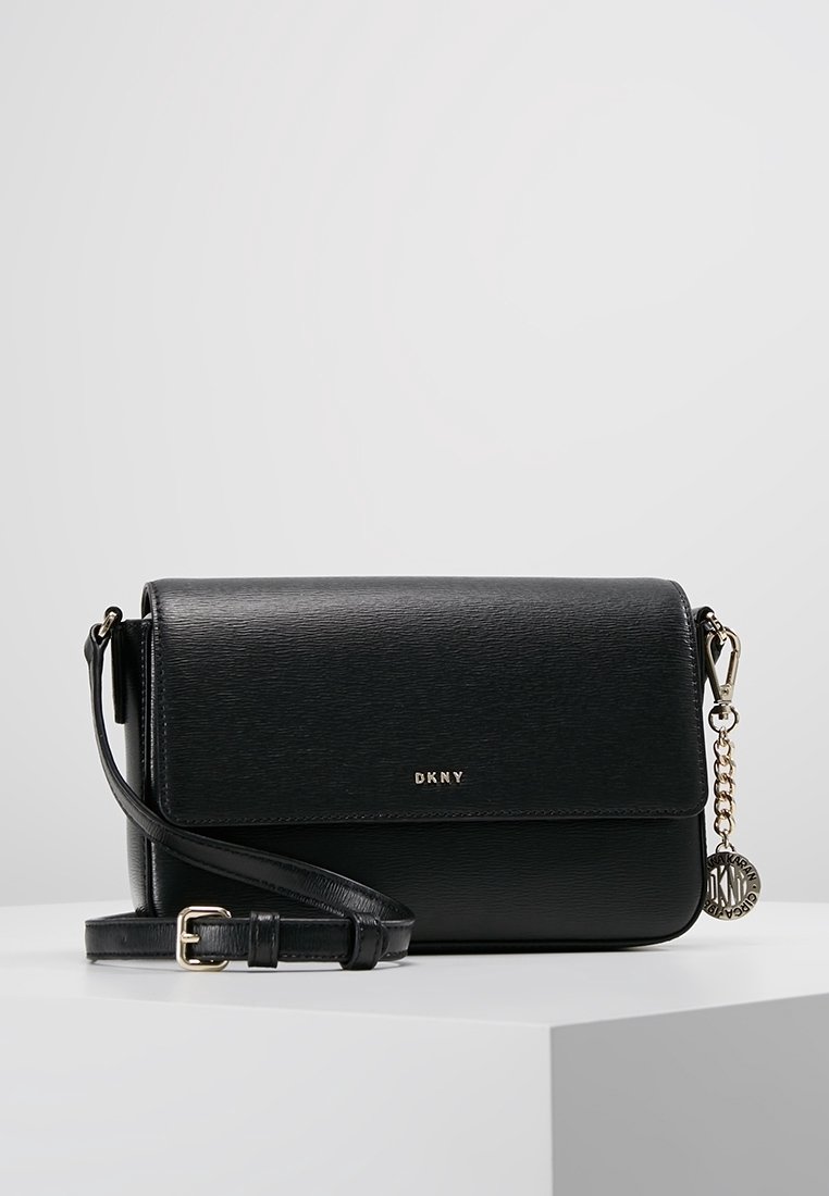 Black leather crossbody bag with textured finish, gold hardware, adjustable strap, and a decorative DKNY charm attached.