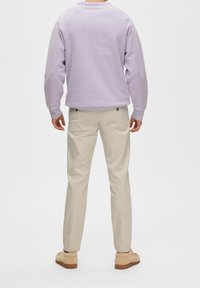 Sweatshirt violet clair avec des manches raglan, chinos beiges et chaussures en suedine marron clair. La tenue présente une coupe décontractée avec des détails minimaux.