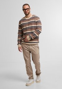 Maglione lavorato a maglia con strisce orizzontali in marrone, beige e blu navy; abbinato a pantaloni beige e sneakers color crema. Tessuto testurizzato.