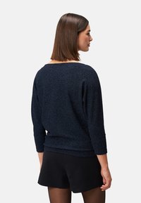 Dunkelblauer, strukturierter Pullover mit Dreiviertelärmeln und lockerer Passform, von hinten gezeigt, kombiniert mit schwarzen Shorts.