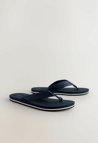 Navy blue flip-flops with textured straps, rubber soles, white and red accents along the edges, and a flat, minimalist design.